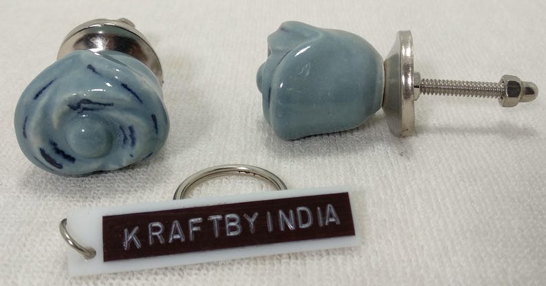 May include: Two blue ceramic rose-shaped drawer knobs with silver hardware. The knobs are attached to a white tag with the text "KRAFTBY INDIA".