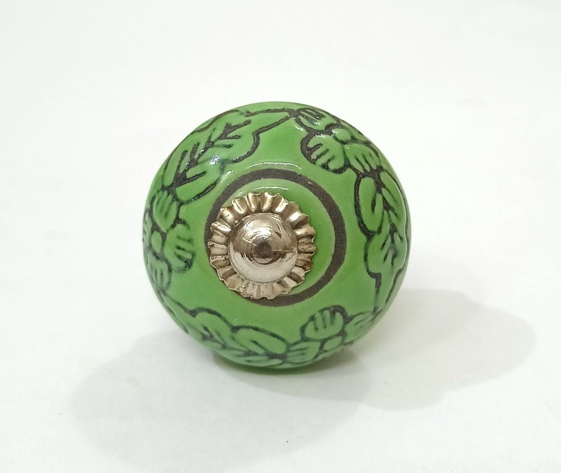 May include: Green ceramic knob with a floral design and a gold metal center.
