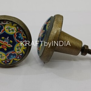 May include: Two antique brass cabinet knobs with a colorful floral design on the front. The knobs have a screw-on base.