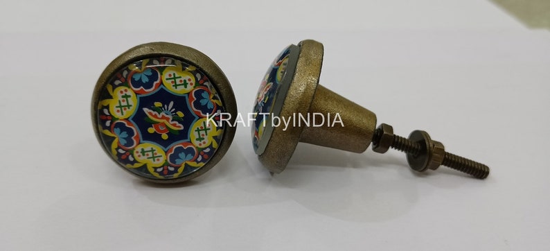 May include: Two antique brass cabinet knobs with a colorful floral design on the front. The knobs have a screw-on base.