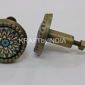 May include: Two antique brass cabinet knobs with a floral design. The knobs have a round base with a raised edge and a screw-on stem. The floral design is in shades of blue, yellow, and white.