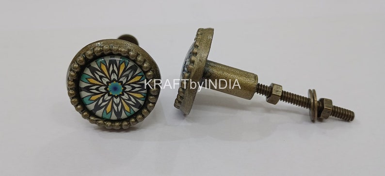 May include: Two antique brass cabinet knobs with a floral design. The knobs have a round base with a raised edge and a screw-on stem. The floral design is in shades of blue, yellow, and white.