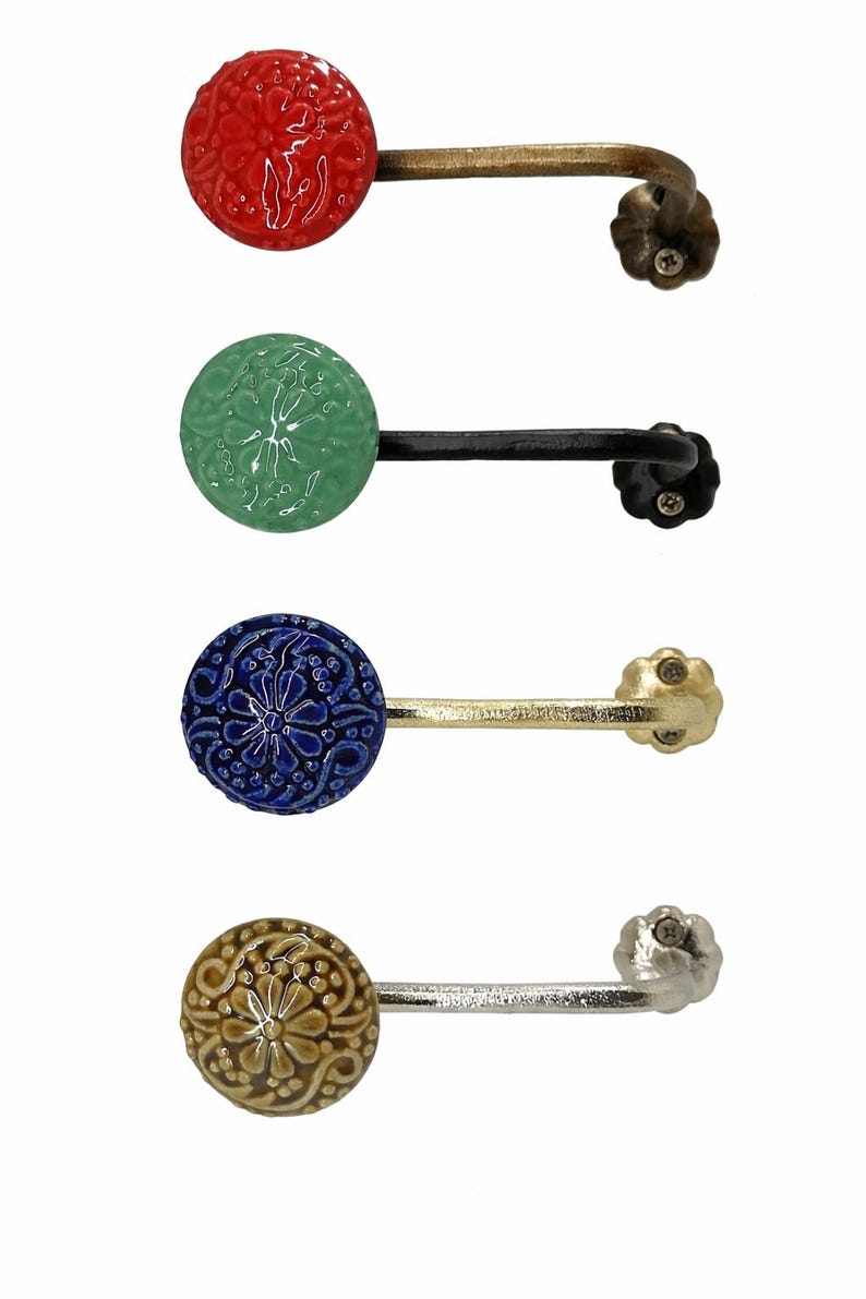 Puede incluir: Cuatro ganchos de pared decorativos con pomos redondos de cer&aacute;mica texturizada en rojo, verde, azul y beige. Cada gancho tiene un brazo de metal curvado y una base decorativa en forma de flor. Ideales para colgar objetos.