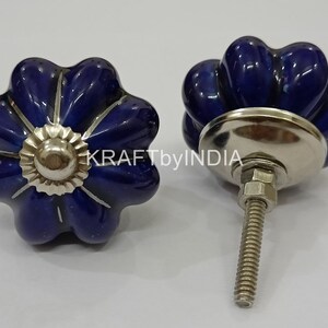 May include: Two blue ceramic cabinet knobs with a silver base and screw. The knobs are shaped like a flower with five petals.
