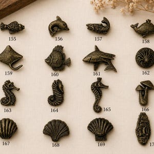 Può includere: Una collezione di sedici pomelli per mobili in metallo color bronzo a forma di creature marine ed elementi naturali, numerati da 155 a 170. I design includono vari pesci, un delfino, una balena, una razza, cavallucci marini, conchiglie e funghi.