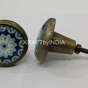 May include: Two antique brass cabinet knobs with a blue and green floral design. The knobs have a round base and a screw-on stem.