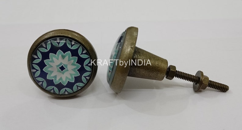 May include: Two antique brass cabinet knobs with a blue and green floral design. The knobs have a round base and a screw-on stem.