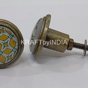May include: Two antique brass cabinet knobs with a yellow and green floral design. The knobs have a round base and a screw-on attachment.