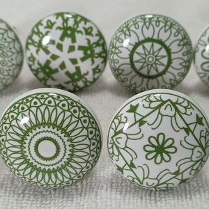 May include: Eight white ceramic knobs with green geometric designs. The knobs have a shiny finish and are perfect for adding a touch of style to any room.