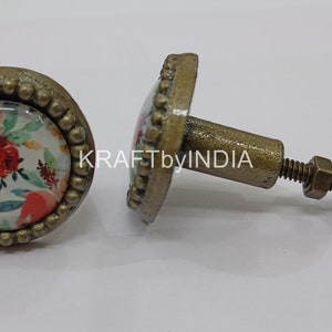 May include: Two round, antique gold cabinet knobs with a floral design. The knobs have a raised beaded edge and a screw-on back.