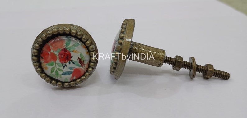 May include: Two round, antique gold cabinet knobs with a floral design. The knobs have a raised beaded edge and a screw-on back.