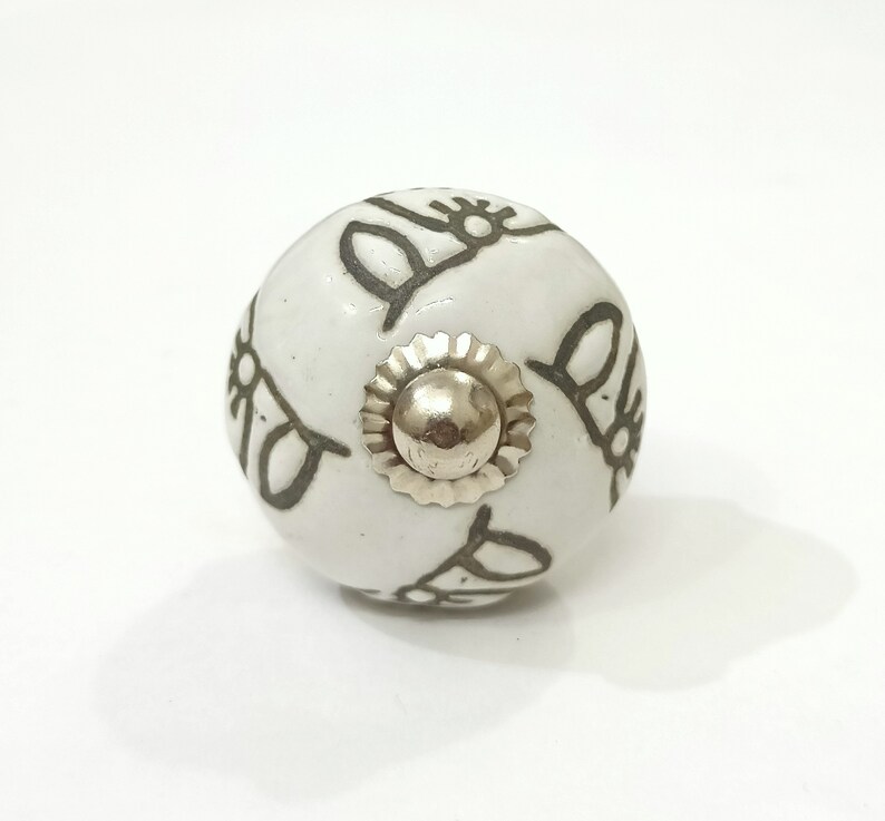 May include: White ceramic knob with a silver metal center and a gray design of stylized flowers.