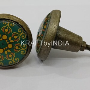 May include: Two green and gold patterned cabinet knobs with a brass finish. The knobs have a round base and a screw-on stem.