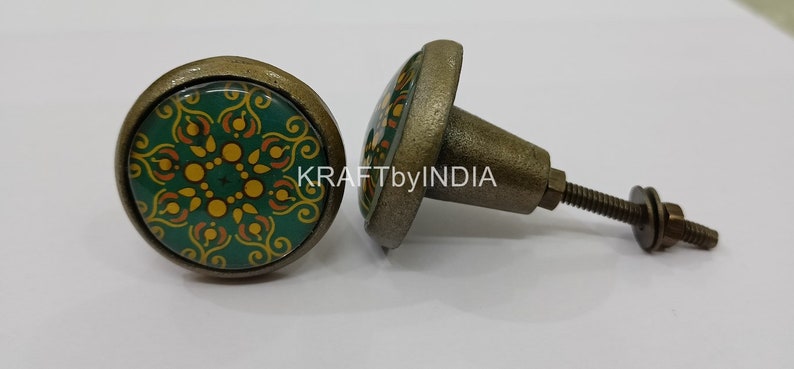 May include: Two green and gold patterned cabinet knobs with a brass finish. The knobs have a round base and a screw-on stem.