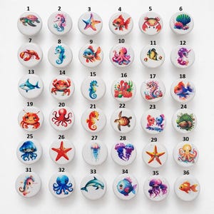 May include: A collection of 36 round cabinet knobs with various sea creature designs. Each knob features a different colorful illustration of marine life, including turtles, seahorses, starfish, fish, crabs, and jellyfish. The knobs are white with a glossy finish.