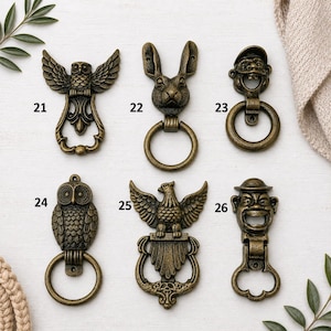 Puede incluir: Una colección de seis aldabas antiguas de color bronce. Los diseños incluyen un búho, un conejo, un hombre con sombrero, un águila y una cara sonriente. Cada aldaba tiene un anillo.
