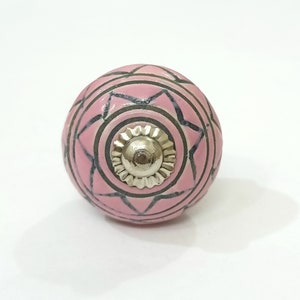 May include: Pink ceramic knob with a black and white geometric design and a silver metal center.