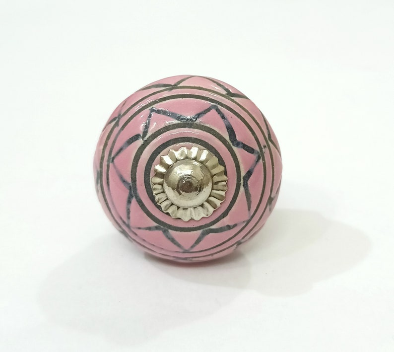 May include: Pink ceramic knob with a black and white geometric design and a silver metal center.