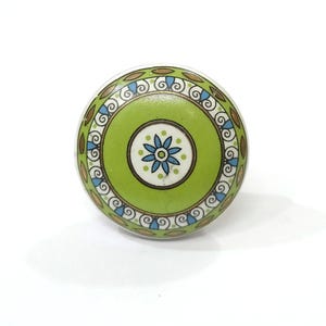 May include: A round, decorative cabinet knob with a green center featuring a blue and white floral design. The knob is encircled by a green, brown, and blue patterned border, adding a touch of color and detail.