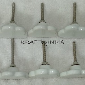 Peut inclure: Dix boutons de porte en c&eacute;ramique blanche en forme de fleur avec des vis argent&eacute;es. Les boutons sont dispos&eacute;s en deux rang&eacute;es de cinq.