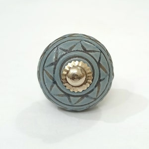 May include: A blue ceramic knob with a geometric pattern and a gold metal center. The knob is round and has a smooth surface.