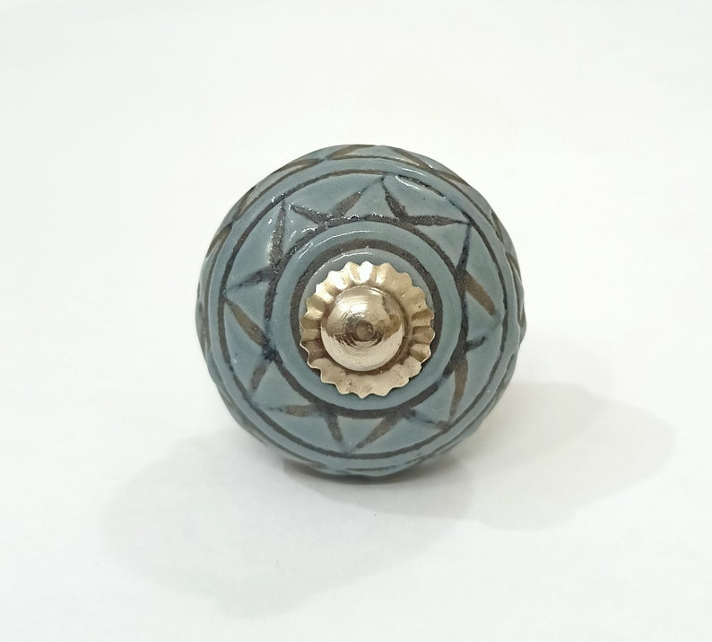 May include: A blue ceramic knob with a geometric pattern and a gold metal center. The knob is round and has a smooth surface.