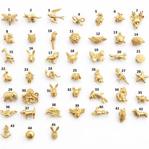 May include: A collection of small, gold-colored metal charms in various animal and object shapes. The charms include a dragonfly, dinosaur, bird, bow, seahorse, bee, deer, squirrel, rabbit, and more. These charms are likely for jewelry making or crafting.