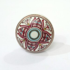 Peut inclure: Un bouton rond en c&eacute;ramique avec un motif floral rose, bleu et or. Le bouton a un fond blanc et une bordure dor&eacute;e.