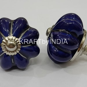 May include: Two blue ceramic cabinet knobs with silver accents. One knob is a flower shape with a silver centre and the other is a round knob with a silver base and screw.