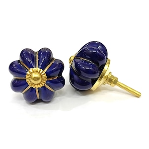 May include: Two navy blue ceramic cabinet knobs with a flower design. The knobs have a gold center and gold accents. The hardware is gold-colored. The knobs are for furniture and home decor.