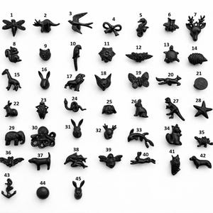 Puede incluir: Una colección de 45 pomos de armario decorativos negros en varias formas de animales y objetos. Los pomos incluyen una libélula, un dinosaurio, una golondrina, un lazo, un caballito de mar, una abeja, una cabeza de ciervo, una ardilla, una cara de gato, un loro, una flor y una mariposa.