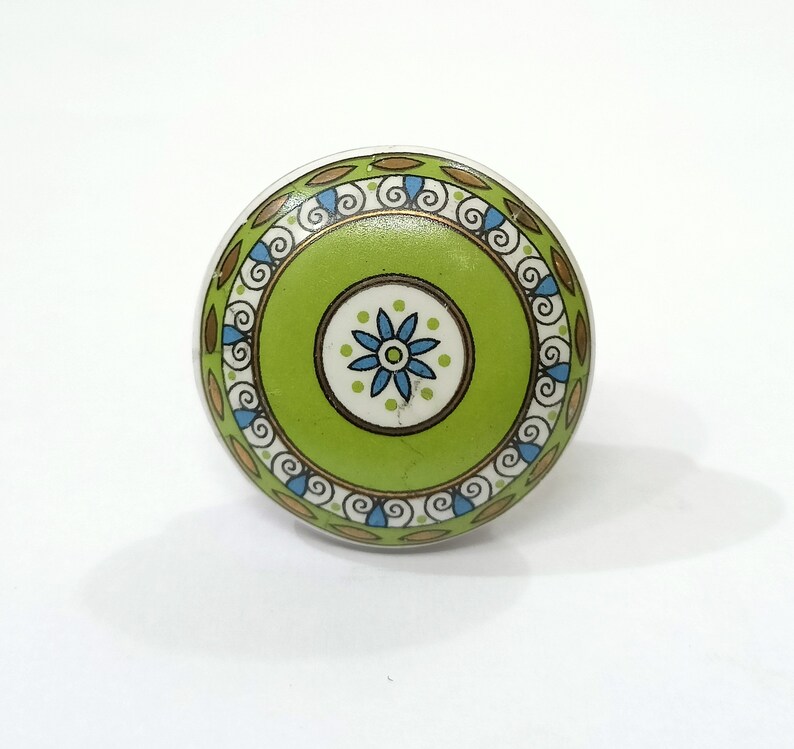 Peut inclure: Un bouton en c&eacute;ramique vert avec un motif floral blanc et or. Le bouton a une bordure d&eacute;corative avec des volutes et des feuilles.