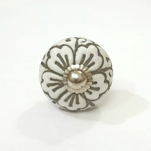 May include: White ceramic knob with a floral design in gray. The knob has a silver metal center.