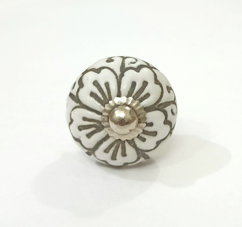 May include: White ceramic knob with a floral design in gray. The knob has a silver metal center.