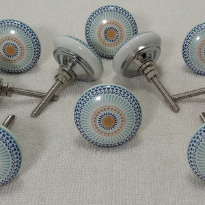 May include: Set of ten ceramic cabinet knobs with a blue, white, and gold geometric pattern. Each knob has a silver screw.