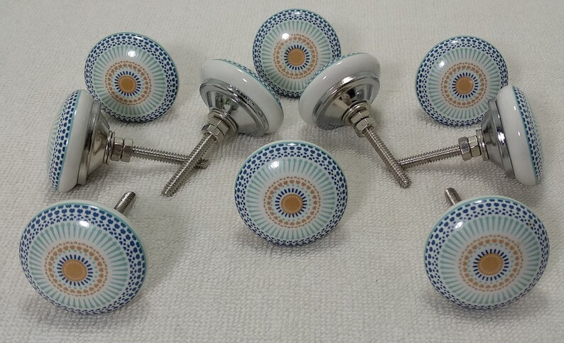 May include: Set of ten ceramic cabinet knobs with a blue, white, and gold geometric pattern. Each knob has a silver screw.