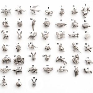 Puede incluir: Una colección de pequeños dijes metálicos plateados en varias formas de animales y objetos. Los dijes incluyen una libélula, un dinosaurio, un pájaro, un lazo, un caballito de mar, una abeja, un ciervo, un oso, un gato, un loro, una flor, alas, una tortuga, un erizo, una jirafa, un conejo, un león, un zorro, una mariposa, un zorro, una estrella de mar y más.