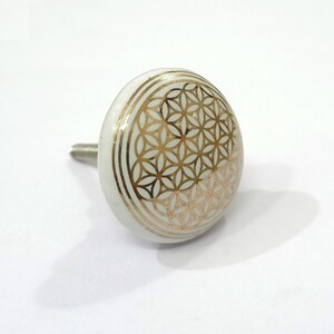 Peut inclure: Bouton de porte en c&eacute;ramique blanche avec un motif g&eacute;om&eacute;trique dor&eacute;. Le motif est un motif de fleur de vie.