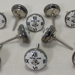 May include: Eight silver and white ceramic clock-face cabinet knobs with black Roman numeral markings and the text "POTTER-STONE".