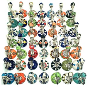 May include: A selection of 49 ceramic wall hooks with metal fixings. Each hook has a unique, hand-painted design in various colours, including blue, orange, green, and white. The hooks are numbered 1-49 and are arranged in rows.