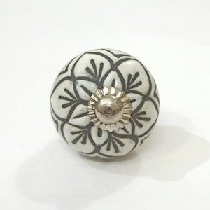 May include: White ceramic knob with a black floral design. The knob has a silver metal center.