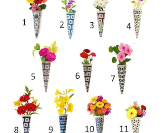 May include: A collection of eleven cone-shaped ceramic vases, each filled with a different arrangement of colorful flowers. The vases feature various patterns and designs, including floral and geometric motifs. The vases are displayed against a white background.