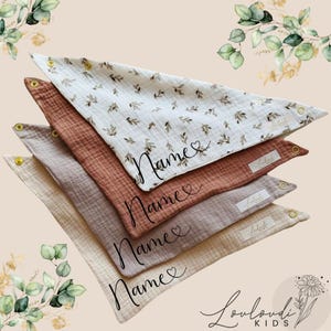 Könnte beinhalten: Vier stapelbare Musselin-Babyspucktücher in Beige, Hellrosa, Hellbraun und Weiß mit einem Blumenmuster. Jedes Spucktuch hat an jeder Ecke eine goldene Öse und das Wort "Name" in schwarzer Kursivschrift mit einem Herzsymbol.