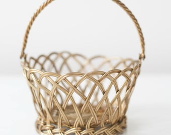 May include: A small, gold-colored wire basket with a woven design and a handle. The basket is empty.