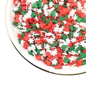 May include: A white bowl filled with red, green, and white sprinkles. The sprinkles are shaped like snowflakes, hearts, and stars.