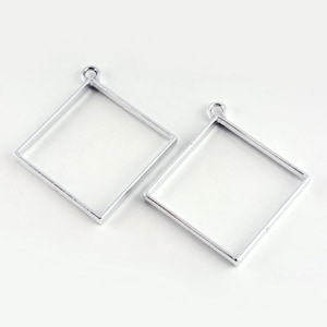 May include: Two silver metal square pendant frames with a loop at the top for hanging.