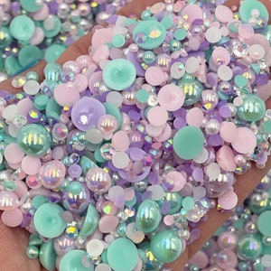 May include: A mix of pastel-colored resin cabochons, pearls, and iridescent rhinestones. The cabochons are in shades of pink, purple, and teal. The pearls are white and iridescent. The rhinestones are clear and iridescent.