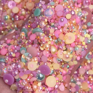 May include: A mix of pastel-colored beads, pearls, and flatback rhinestones. The mix includes light pink, light blue, light yellow, and light purple.