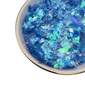 May include: A white bowl with a gold rim filled with iridescent blue glitter flakes.
