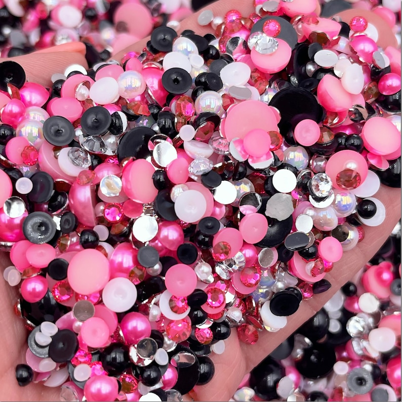Pode incluir: Um grande sortimento de strass e p&eacute;rolas redondas e facetadas de cor rosa, branca e preta.